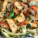 close up of chicken, sun dried tomatoes and mushroom cream sauce over spinach fettuccine