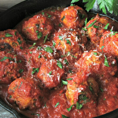 black skillet with meatballs in marinara garnished with parsley