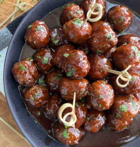 grape jelly meatballs recipe - black bowl with a pile of meatballs blanketed in sweet spicy sauce