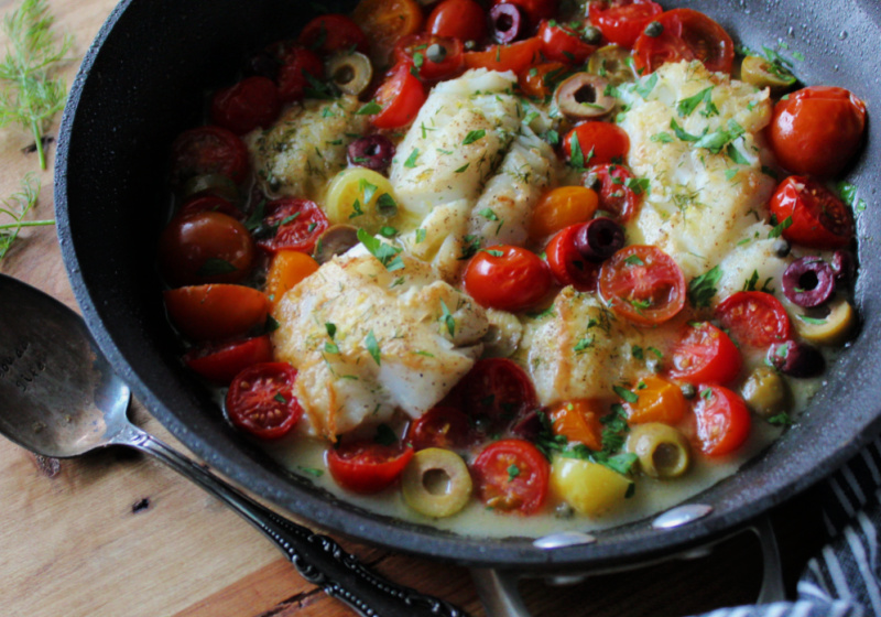 closeup of mediterranean baked fish ins skillet with tomatoes, olives and capers