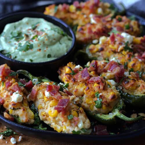 black plate with mexican street corn jalapeno poppers and a bowl of avocado creme.
