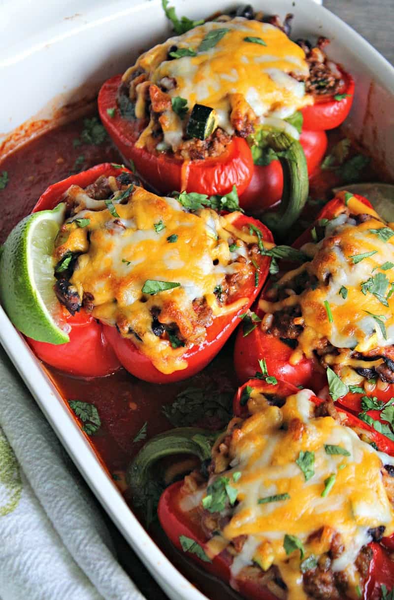 Stuffed red bell peppers topped with melted cheese in enchilada sauce in white casserole dish