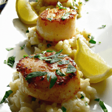 Seared sea scallops on a bed of risotto garnished with lemon wedges