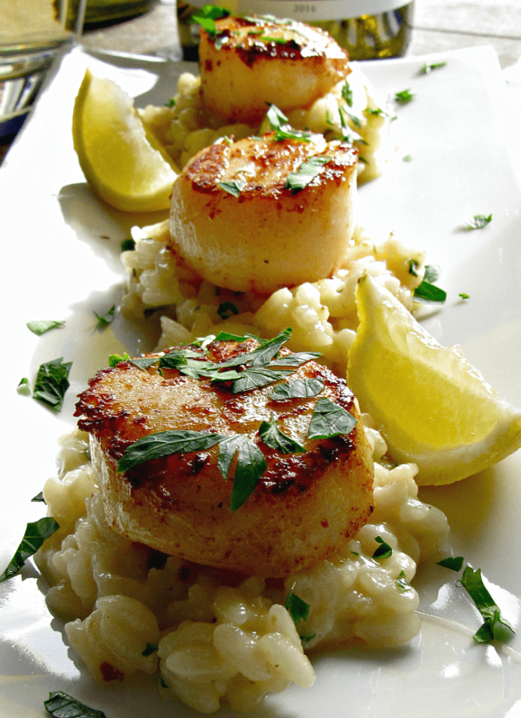 Seared sea scallops on a bed of risotto garnished with lemon wedges