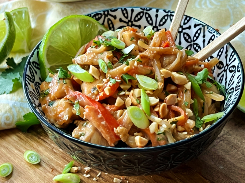 black bowl with spicy chicken pad thai garnished wtih slivered green onions