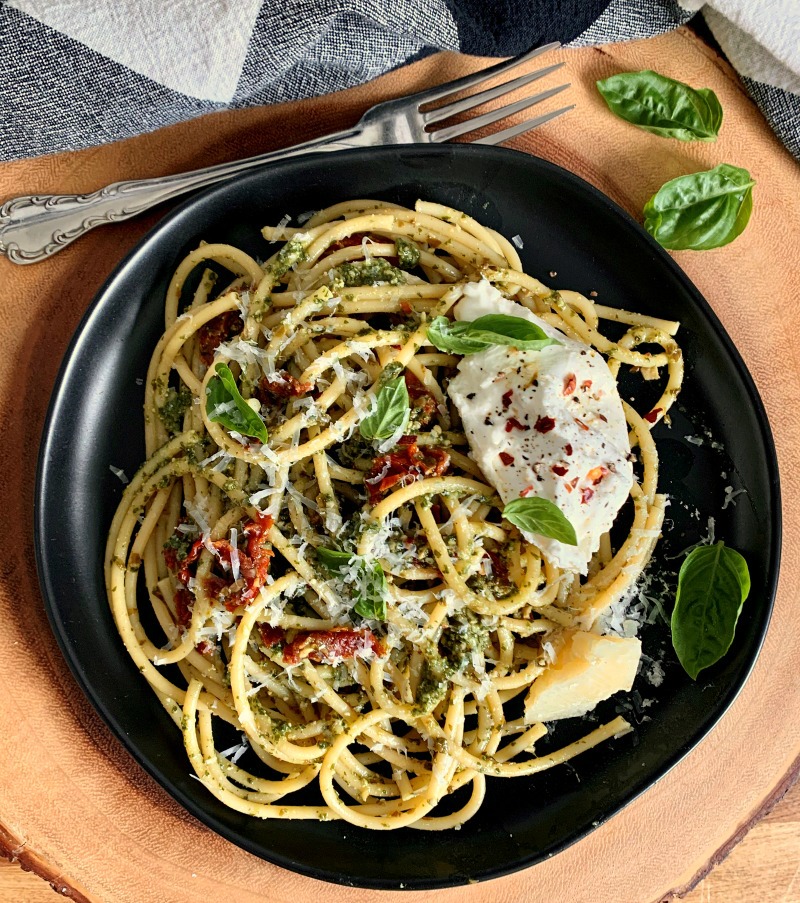 black plate of pasta garnished with bail and buratta
