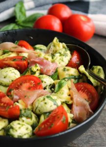 overhead view pesto tortellini salad with sliced tomatoes and prosciutto