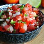 black bowl with pico de gallo and sliced lime in the background