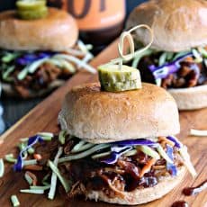 slow cooker beer braised pulled pork ~ side view of slider topped with green and purple shredded cabbage, topped with a pickle.