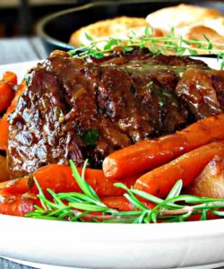 pot roast on white platter with gravy, carrots and potatoes