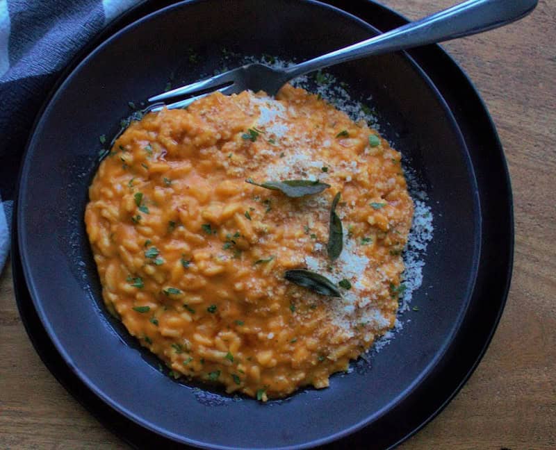 black bowl with pumpkin rice (risotto) garnished with crispy sage leaves