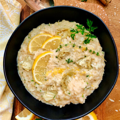 overhead view black bowl with creamy risotto garnished with lemon slices and parsley