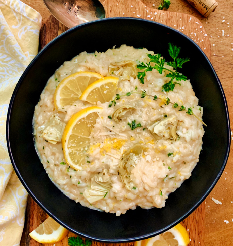 overhead view black bowl with creamy parmesan risotto garnished with lemon slices and parsley
