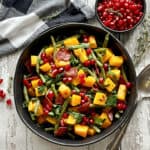 overhead view black bowl with roasted green beans and butternut squash garnished with pomegranate seeds