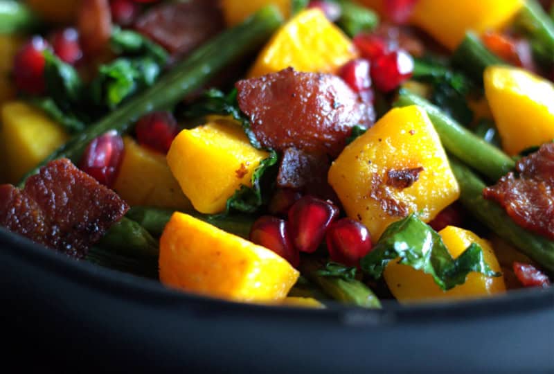 black bowl with roasted green beans and butternut squash garnished with pomegranate seeds
