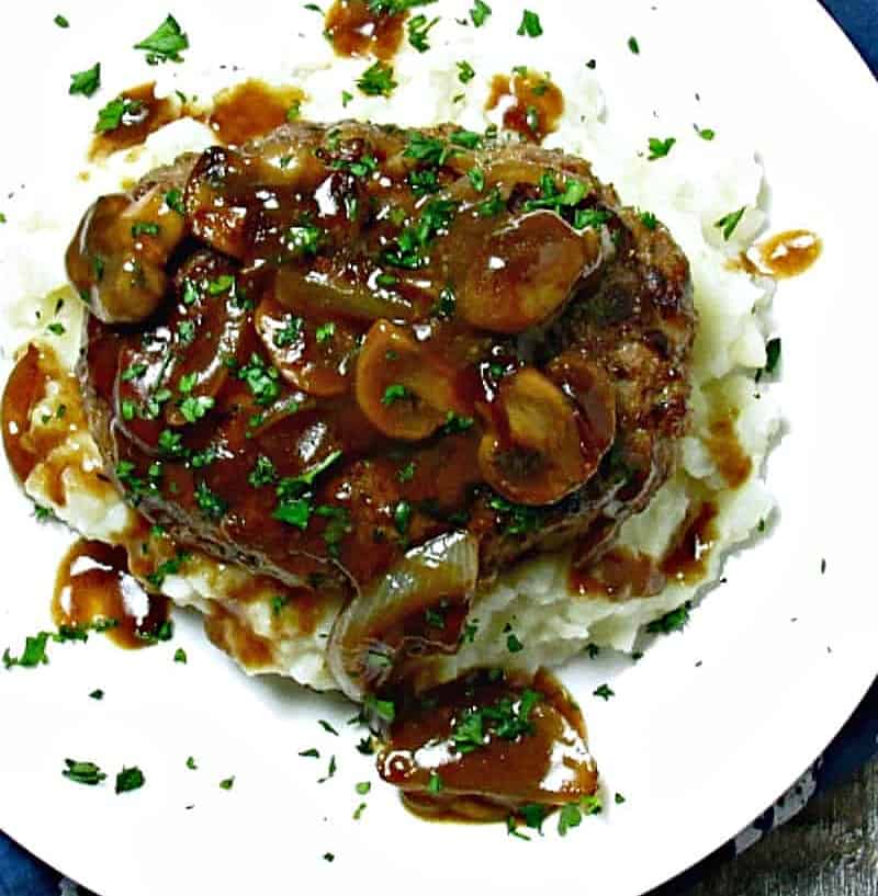 white plate with mashed potatoes topped with salisbury steak patty and mushroom gravy
