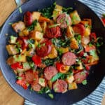 black bowl with sliced smoked sausage, potatoes, peppers and onions