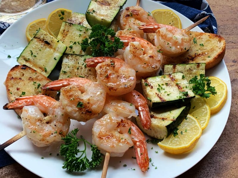 white plate with grilled lemon garlic shrimp, grilled zucchini and lemon wedges