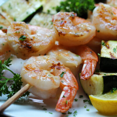 white plate with grilled lemon garlic shrimp skewers, zucchini and grilled bread