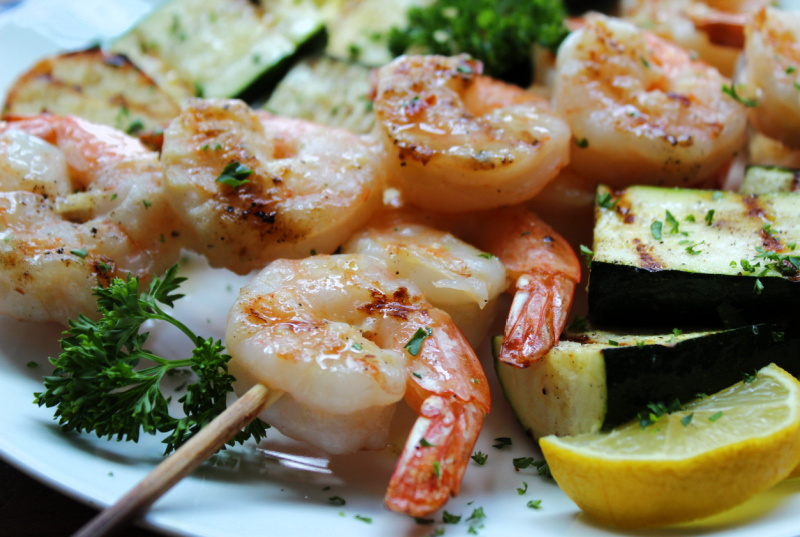 white plate with grilled lemon garlic shrimp skewers, zucchini and grilled bread