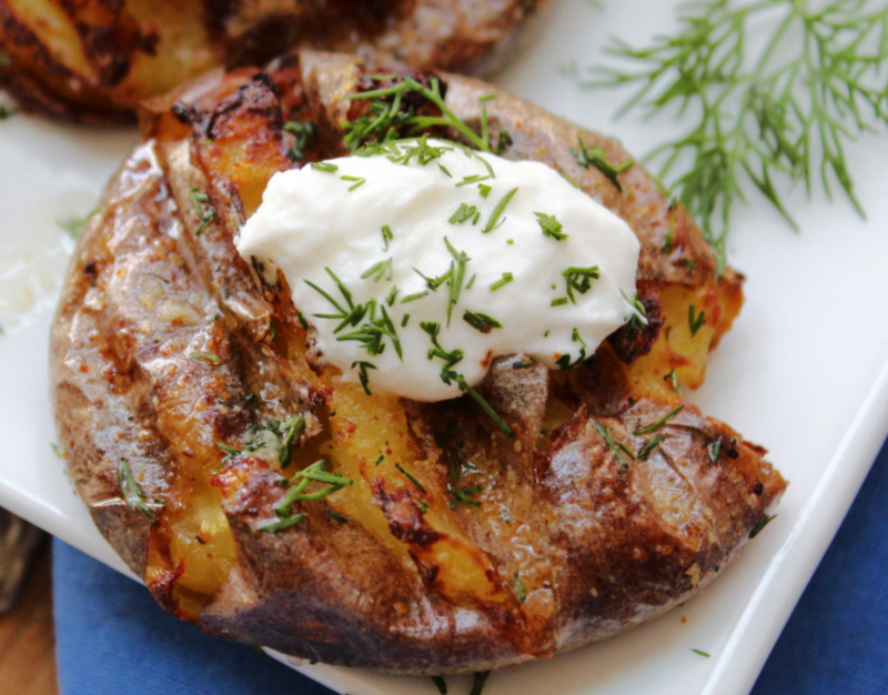 overhead view white plate with air fryer smashed potatoes with a dollop of sour cream