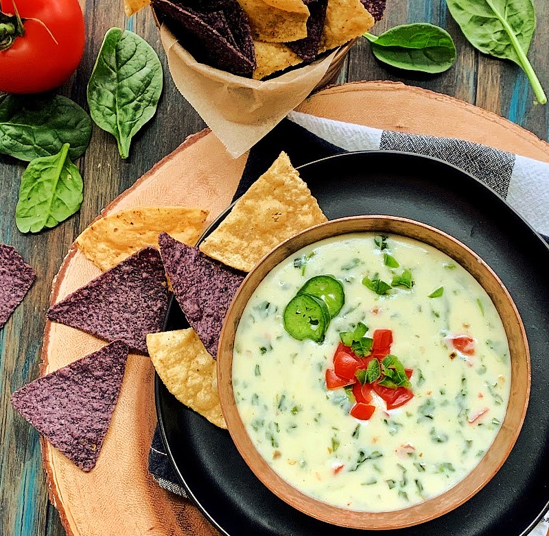 bowl of spinach queso garnished with diced tomatoes and jalapeno