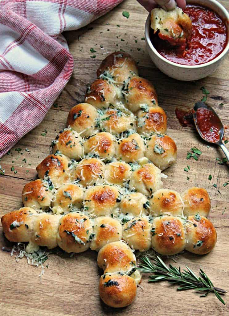 wood board with cheesy pull-apart christmas tree bread and small bowl of marinara for dippin