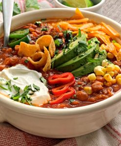 Bowl of turkey lentil chili garnished with cheese, avocado and sour cream
