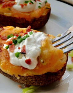 white plate with air fryer twice baked potatoes garnished with sour cream and green onions