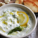 white bowl with Tzatziki Greek Yogurt Sauce garnished with chopped dill