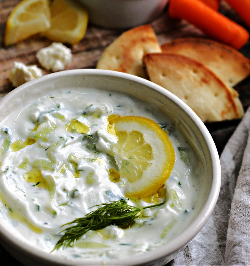 closeup of tzatziki greek yogurt sauce in white bowl garnished with lemon slice