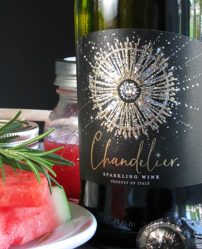 watermelon sparkling wine cocktail ~ chanderlier sparkling wine bottle with jar of watermelon juice and slices of watermelon nearby