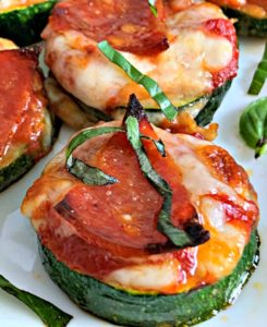 zucchini pizza bites on white plate garnished with sliced basil